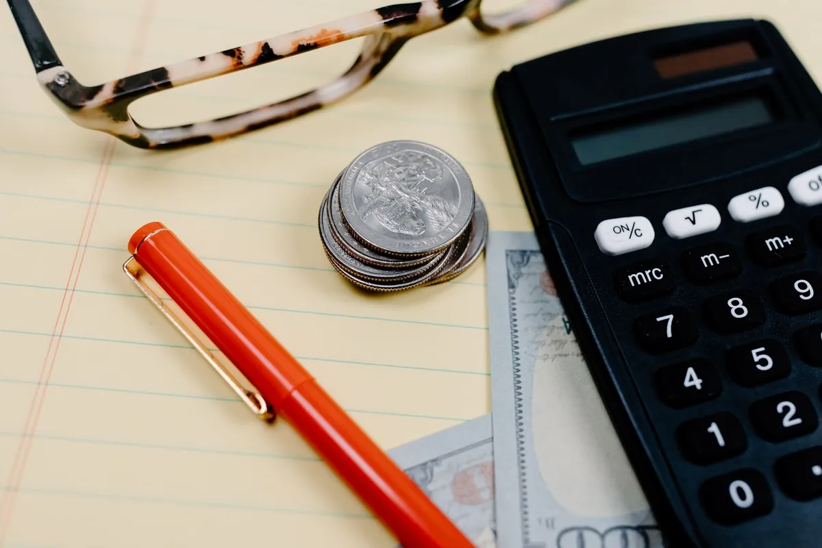 Close-up of a workspace with a calculator, coins, and glasses on a notepad, reflecting silver coin buying.
